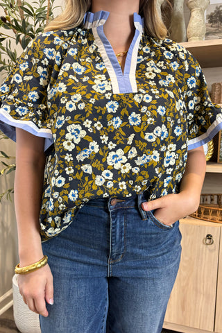 Person wearing a floral blouse with blue jeans indoors.