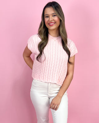 Woman wearing a pink ribbed top and white pants against a pink background
