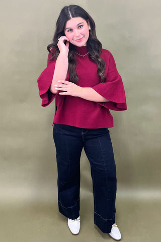 Woman wearing a burgundy top and dark jeans against a beige background