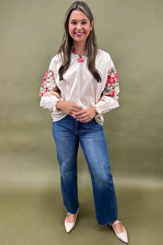 Woman wearing a white blouse with floral embroidery and blue jeans on a green background