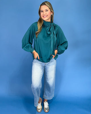 Emerald green satin blouse with a tie neck, long balloon sleeves, and gathered cuffs, shown on model.