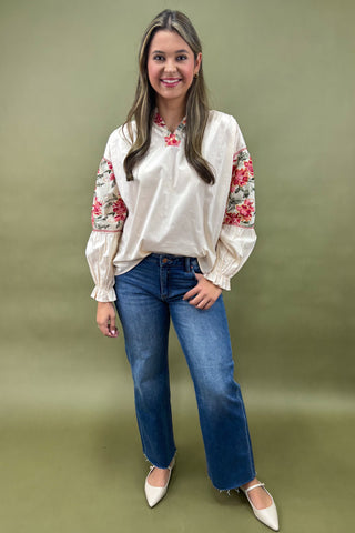 Woman wearing a white blouse with floral sleeves and blue jeans on a green background