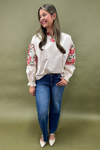 Woman wearing a white blouse with floral sleeves and blue jeans on a green background