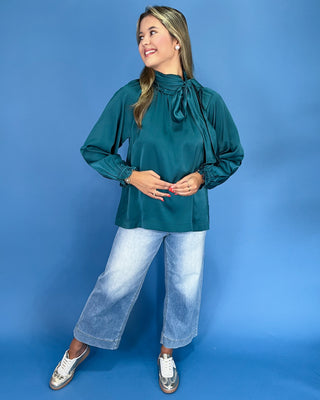 Emerald green satin blouse with a tie neck, long balloon sleeves, and gathered cuffs, shown on model.