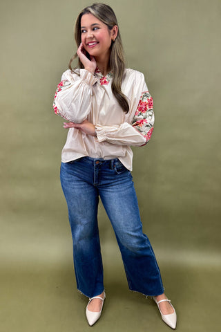 Woman wearing a floral blouse and blue jeans against a green background