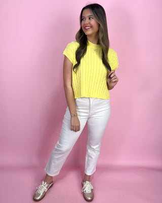 Woman wearing a yellow top and white pants against a pink background