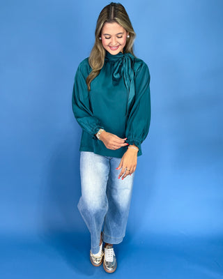 Emerald green satin blouse with a tie neck, long balloon sleeves, and gathered cuffs, shown on model.