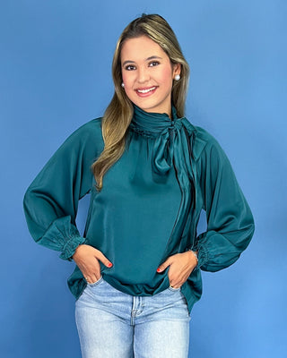 Emerald green satin blouse with a tie neck, long balloon sleeves, and gathered cuffs, shown on model.