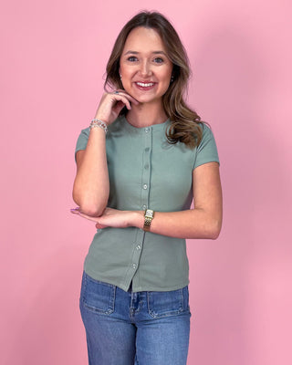 Woman wearing a green shirt and blue jeans against a pink background