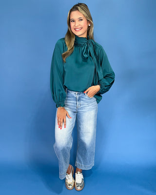 Emerald green satin blouse with a tie neck, long balloon sleeves, and gathered cuffs, shown on model.