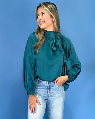 Emerald green satin blouse with a tie neck, long balloon sleeves, and gathered cuffs, shown on model.