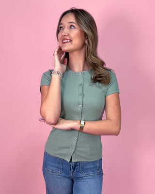 Woman wearing a green shirt and blue jeans against a pink background
