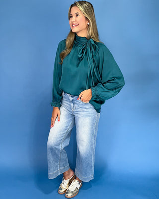 Emerald green satin blouse with a tie neck, long balloon sleeves, and gathered cuffs, shown on model.