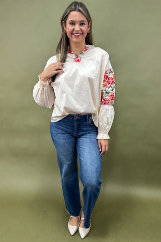Woman wearing a white blouse with floral sleeves and blue jeans against a green background