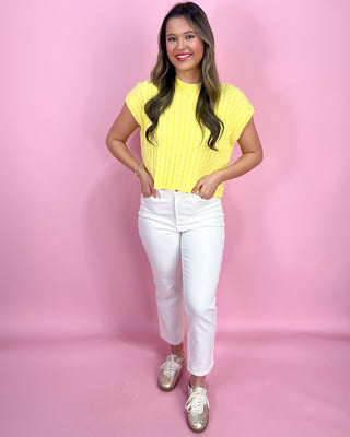 Woman wearing a yellow top and white pants against a pink background