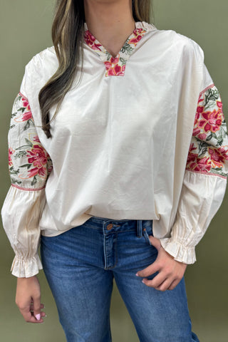 White blouse with floral sleeves and collar worn by a person on a green background