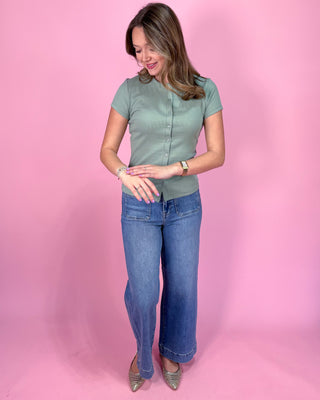 Woman wearing a green top and blue jeans against a pink background