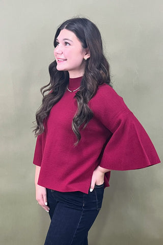 Woman wearing a red blouse with bell sleeves against a beige background