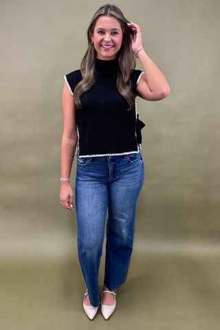Woman wearing a black top with white trim and blue jeans on a beige background