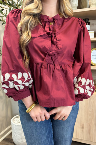 Person wearing a red blouse with white floral patterns and blue jeans indoors.