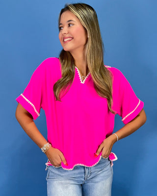 Hot pink top with white whipstitch trim, split neckline, short sleeves, and relaxed fit, shown on model.