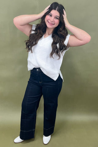 Woman wearing a white top and dark jeans against a green background