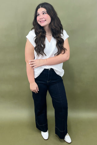 Woman wearing a white blouse and dark jeans against a green background