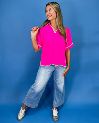 Hot pink top with white whipstitch trim, split neckline, short sleeves, and relaxed fit, shown on model.