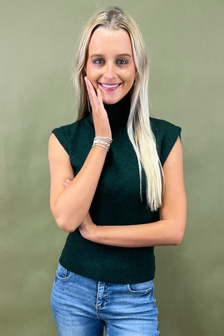 Woman wearing a green sleeveless top and blue jeans against a green background