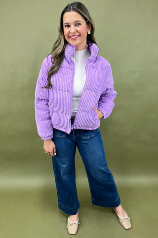 Woman wearing a purple jacket and blue jeans on a green background