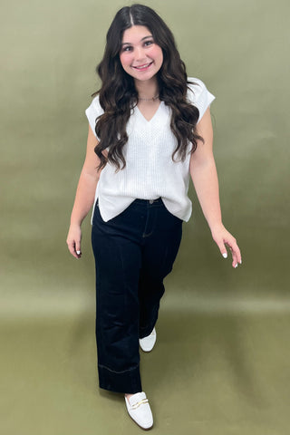 Woman wearing a white top and dark pants against a green background