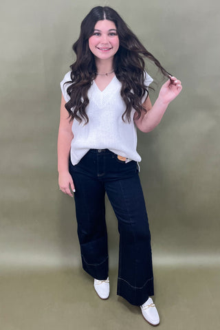 Woman wearing a white top and dark blue jeans against a plain background