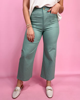 Person wearing teal pants and white shoes on a pink background
