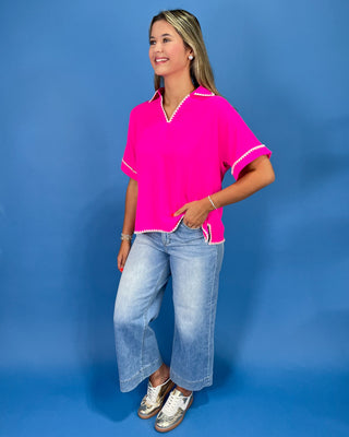 Hot pink top with white whipstitch trim, split neckline, short sleeves, and relaxed fit, shown on model.