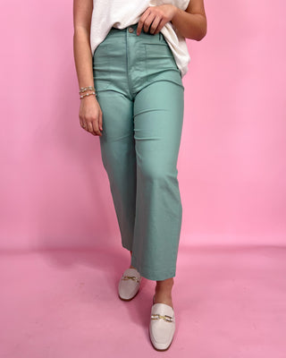 Person wearing teal pants and white shoes on a pink background