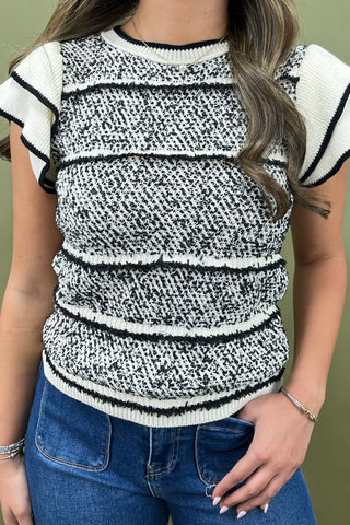 Person wearing a black and white patterned sweater with blue jeans against a green background