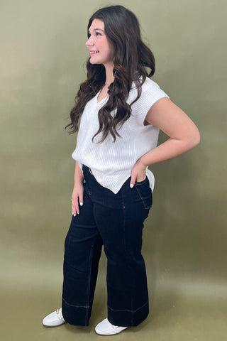 Woman wearing a white top and dark pants against a green background
