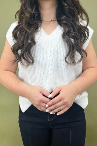 Person wearing a white sleeveless top against a green background