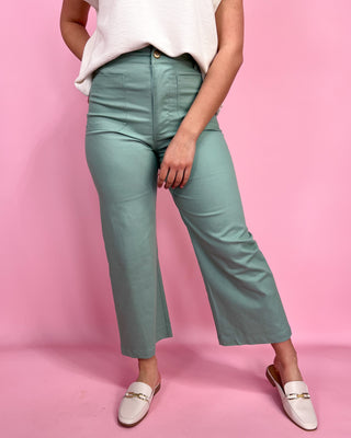 Person wearing teal pants and white shoes on a pink background