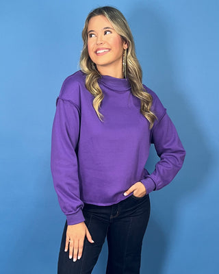 Purple long sleeve mock neck sweatshirt top with a relaxed fit and raw edge details.