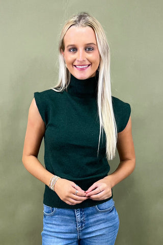 Woman wearing a dark green sleeveless top and blue jeans against a green background
