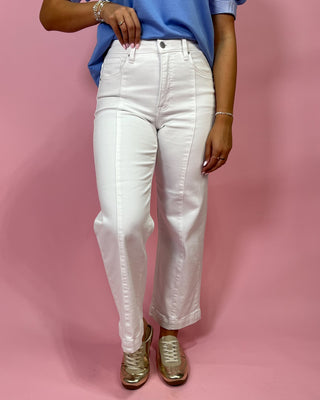 Person wearing white jeans and a blue top on a pink background