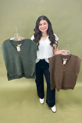 Woman holding two sweater vests against a green background