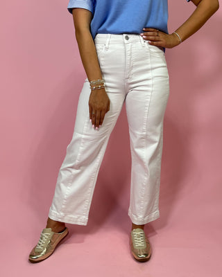 Person wearing white jeans and a blue top on a pink background