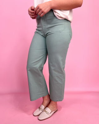 Person wearing light green pants and pink shoes on a pink background