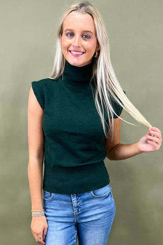 Woman wearing a green turtleneck sweater and blue jeans against a green background