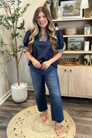 Woman in a navy blue top and jeans standing in a room with decor elements.