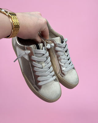 Pair of beige sneakers held by a hand against a pink background