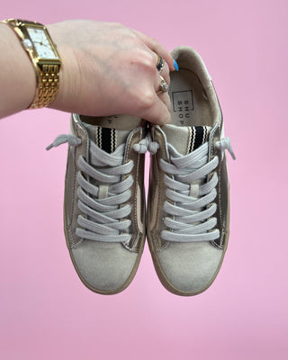 Person holding a pair of light gray sneakers against a pink background