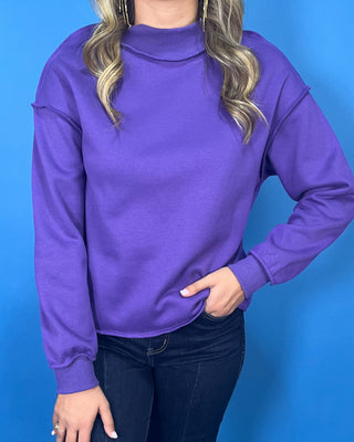 Purple long sleeve mock neck sweatshirt top with a relaxed fit and raw edge details.
